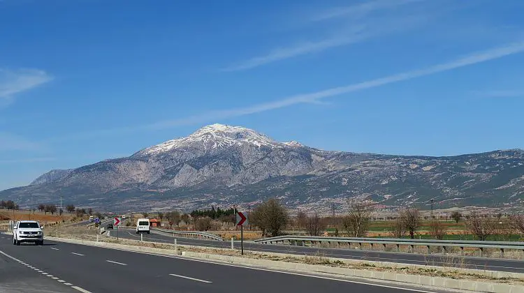 Ein Mietwagen fährt gerade am Straßenrand der Straße von Antalya nach Denizli vorbei. Im Hintergrund ist ein schneebedeckter Berg. 