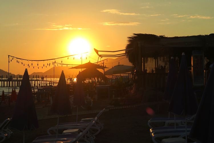 Die orange-rote Sonne geht hinter einer Strandbar in Alanya unter.