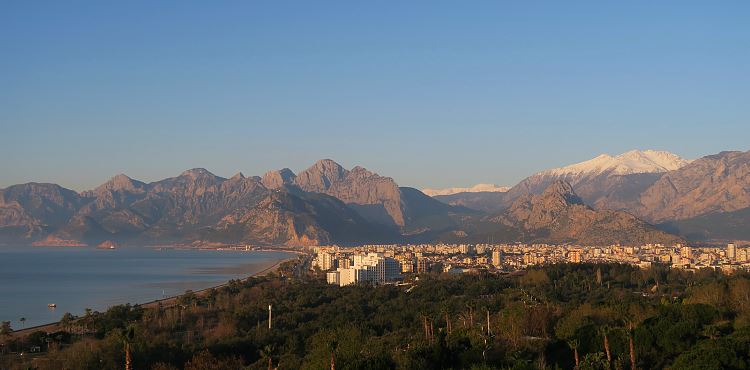 Grüne Palmen und Sonne an der Küste und Schnee auf den Berggipfeln von Antalya. 