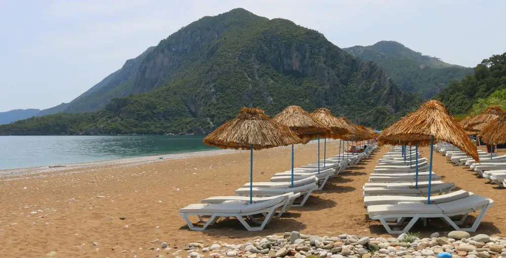 Sandstrand mit Liegestühlen und bewaldeten Bergen