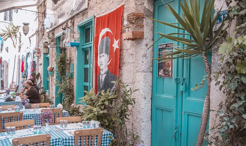 Hauswand mit der türkischen Flagge, einer türkisblauen Türe und einem Restaurant in Alacati