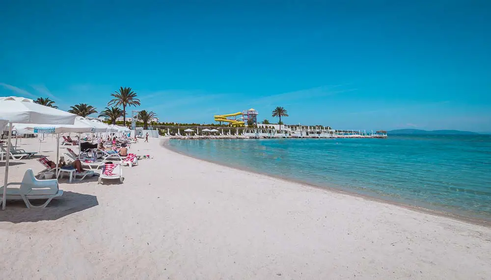 Weißer Sandstrand des Cesme Thermal Resort mit Sonnenliegen, Sonnenschirmen und dem Meer