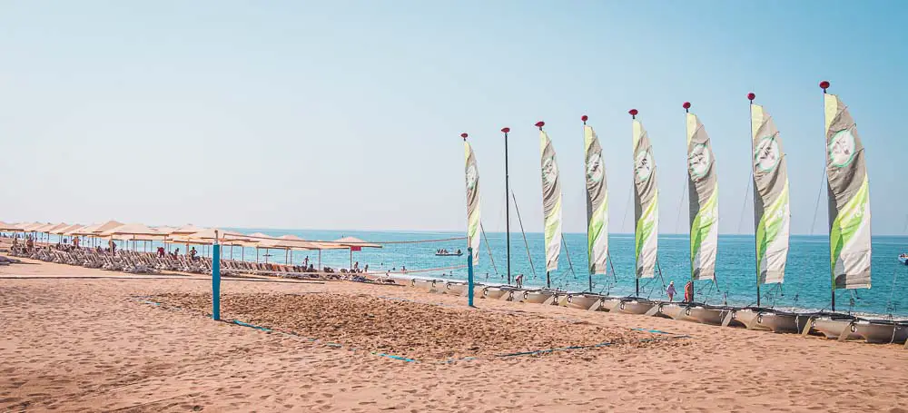 Katamaran-Seegelschiffe, der Beach Volleyballplatz und Sonnenliegen am Strand mit Blick auf das Meer vor dem Paloma Orenda Resort