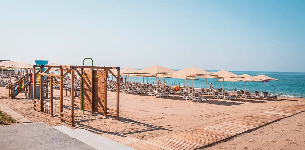 Westlicher Sandstrand im Paloma Orenda Resort mit Sonnenliegen, Sonnenschirmen und einem kleinen Kinderspielplatz